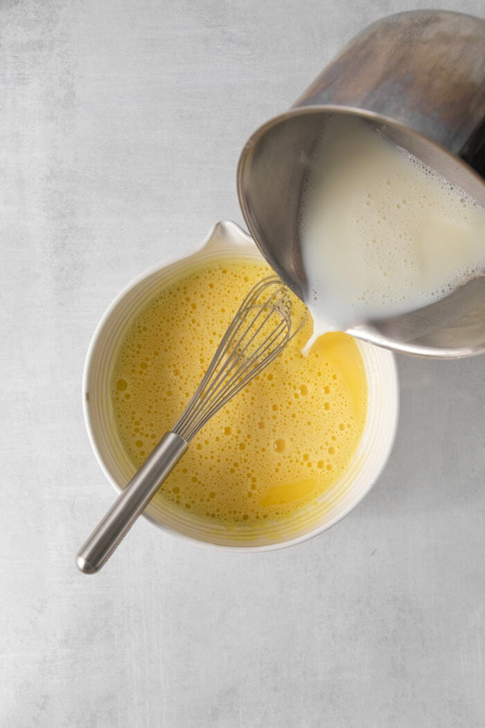 A little warm milk is poured into a bowl of egg yolks to temper them.