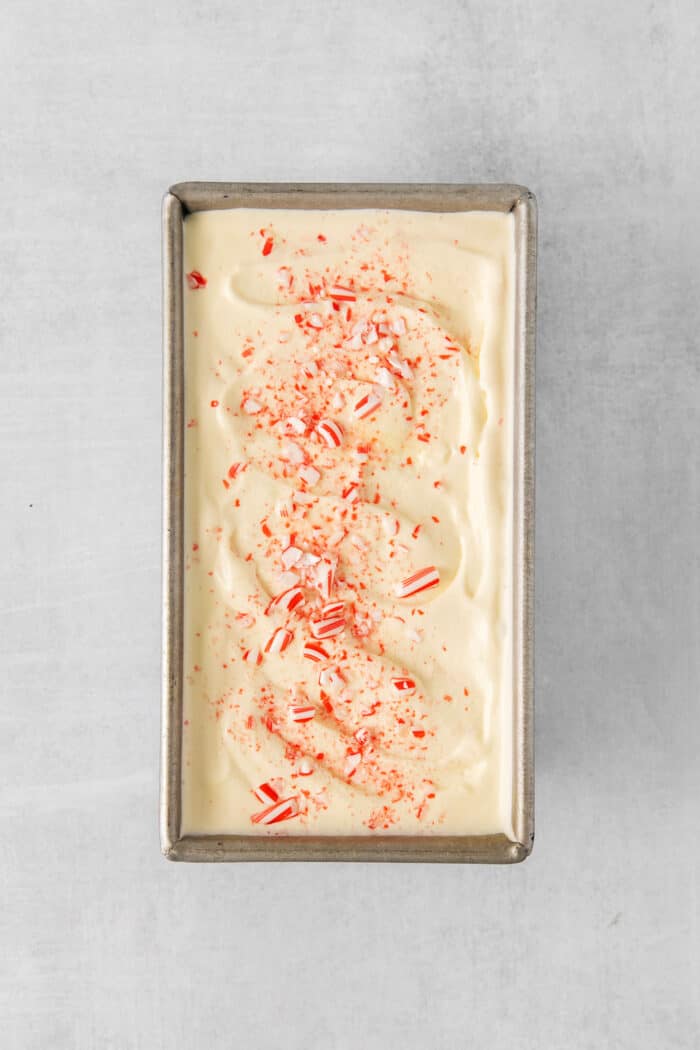 A metal loaf pan holds cream-colored ice cream topped with crushed candy cane pieces.