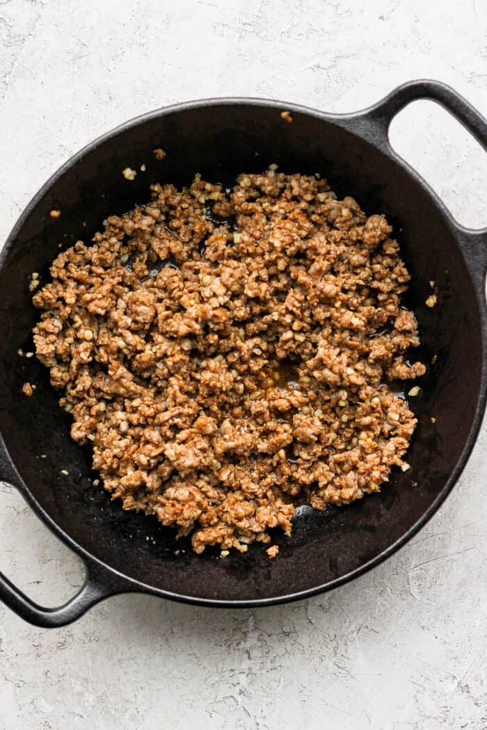 Crumbled chorizo browns in a cast iron skillet.