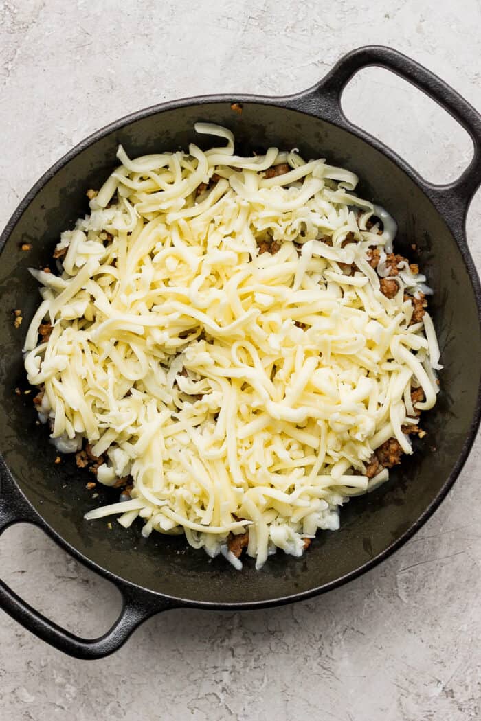 Shredded Jack cheese is layered on top of Oaxaca cheese and chorizo in a cast iron skillet.