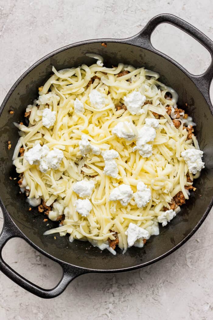 Goat cheese crumbles are layered on top of Jack and Oaxaca cheeses and chorizo in a cast iron skillet.