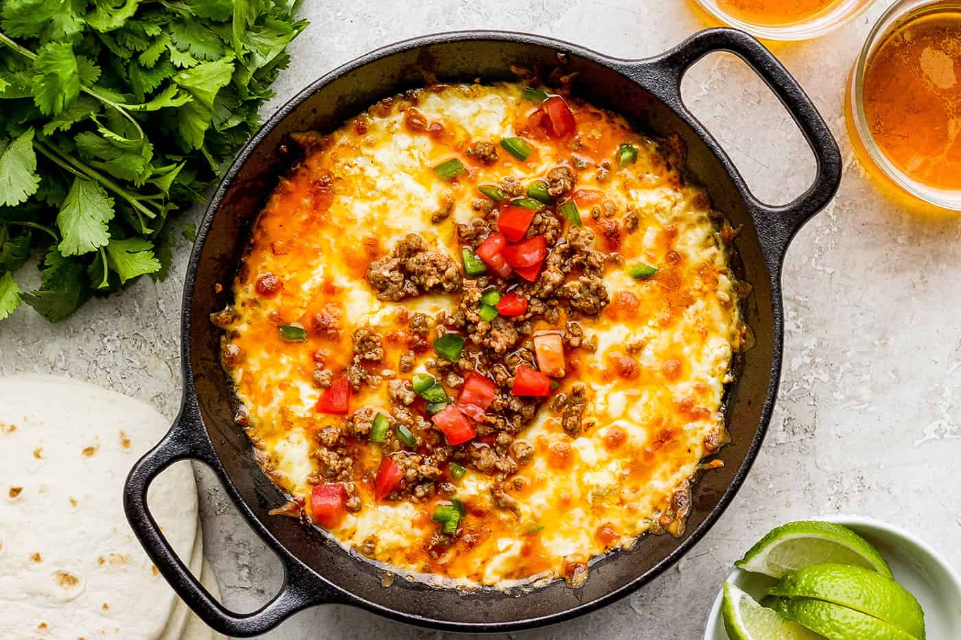 A black cast iron skillet of queso fundido topped with chorizo, tomatoes, and jalapeno.