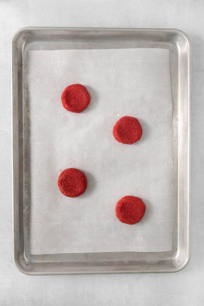 Four red velvet cookies on a baking sheet.