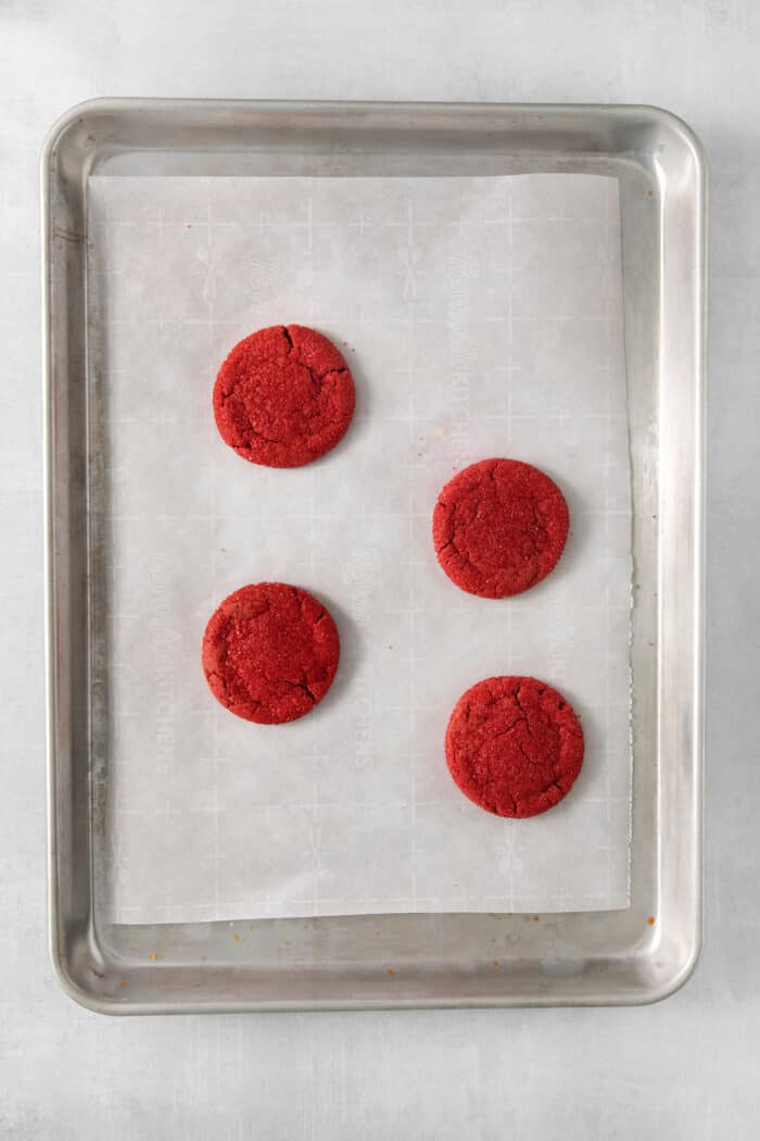 Four red velvet cookies on a baking sheet.