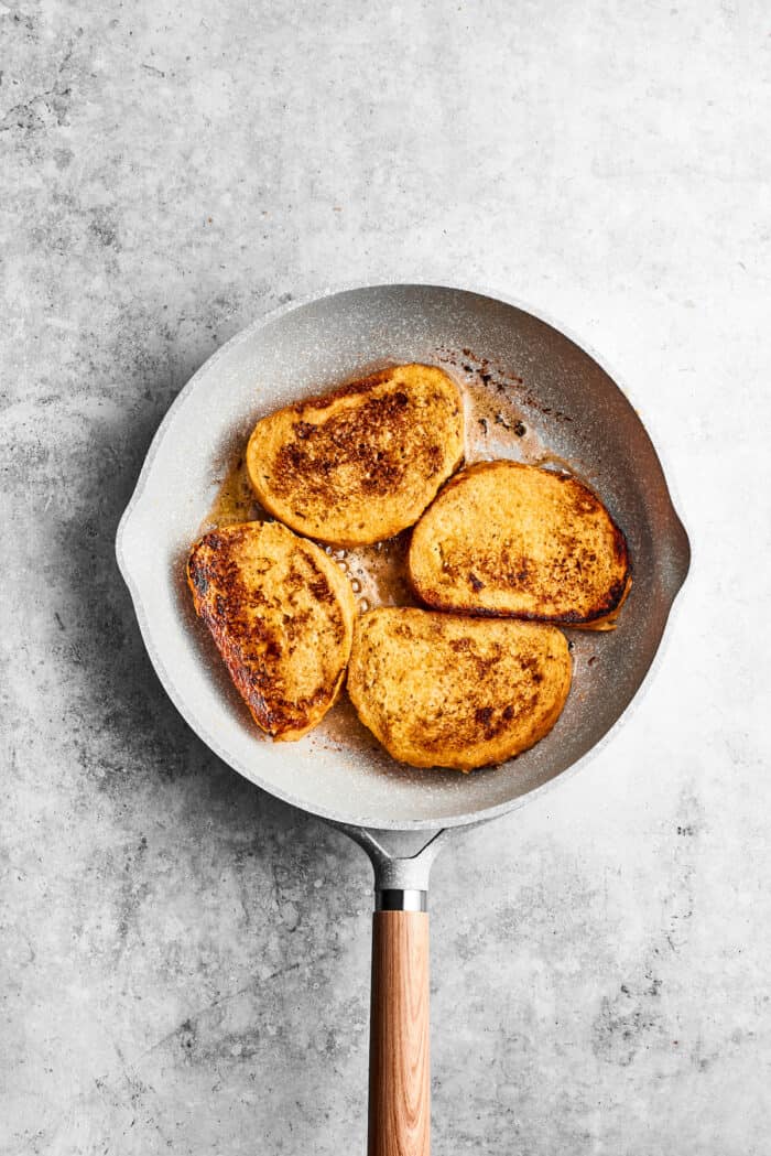 Four pieces of bananas foster French toast cook in a skillet.