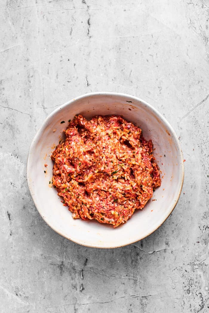 The mix for porcupine meatballs in a white bowl.