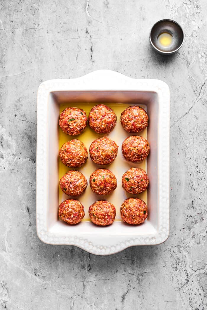 A white baking pan holds 12 uncooked porcupine meatballs.