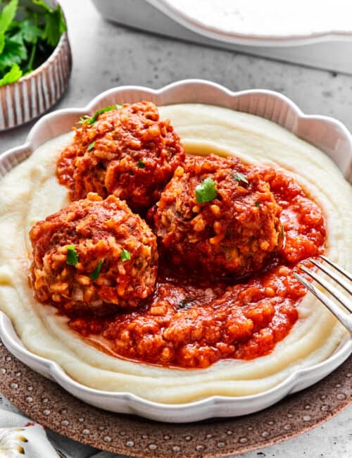 Three porcupine meatballs in tomato sauce on top of mashed potatoes with a fork.