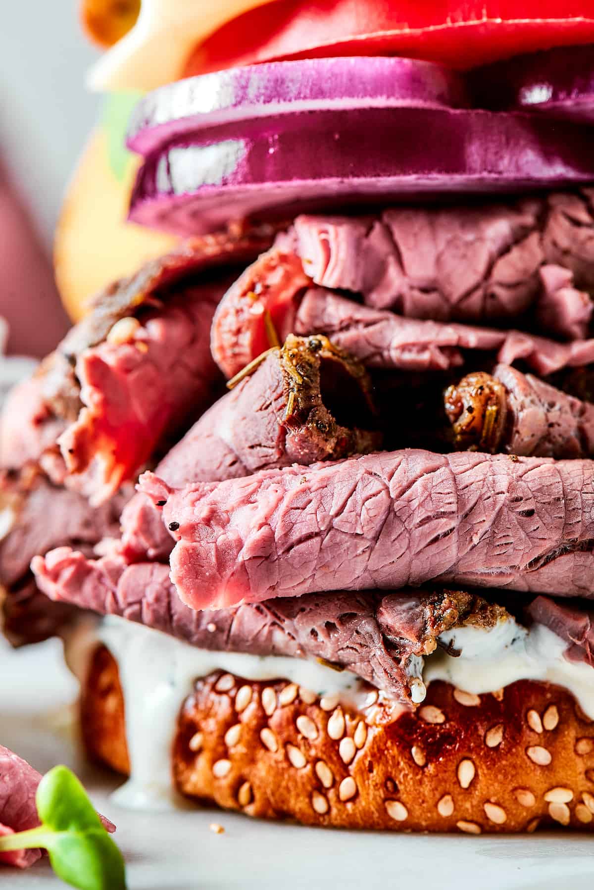 a close-up photo of a piled-high roast beef sandwich with sliced onion and tomato