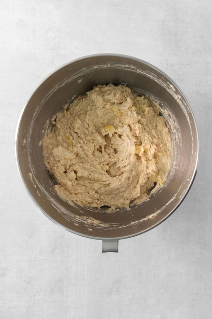 Bananas are added to a metal bowl of batter.