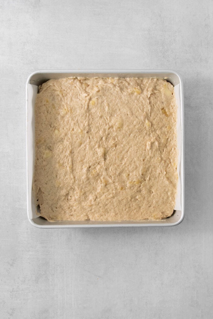 The batter for banana coffee cake is spread out in a metal baking pan.