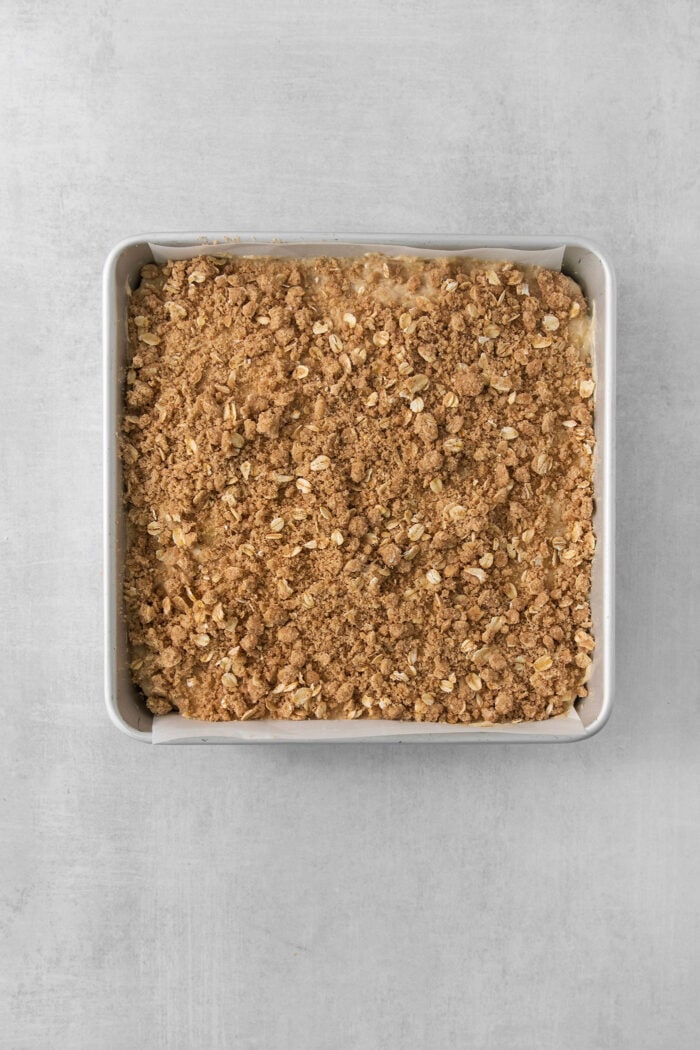 A metal baking pan of streusel-topped banana coffee cake on a white background.