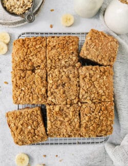 Banana coffee cake is cut into 9 squares with banana slices scatted around them.