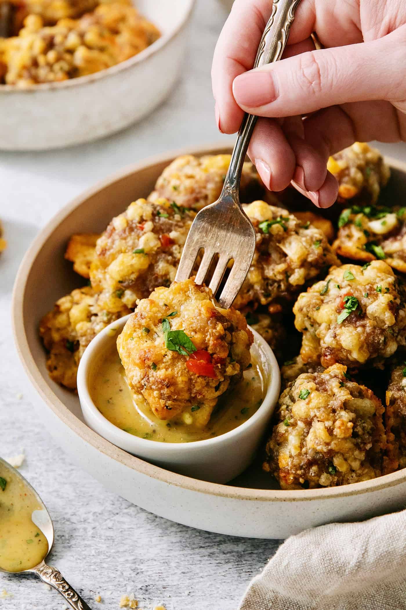 A fork spears a sausage cheese ball and dips it into honey mustard sauce.