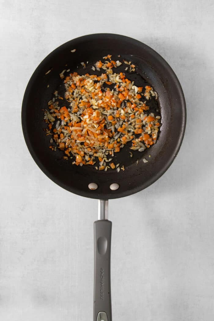 Diced onion, garlic, and red pepper pepper cook in a skillet.