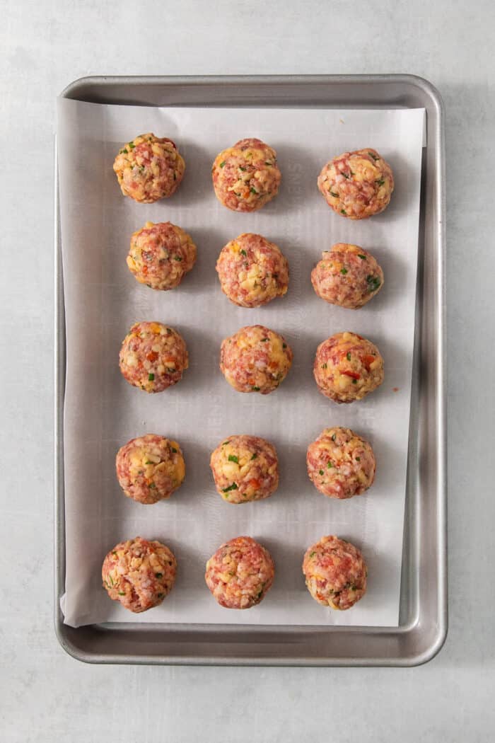 Sausage cheese balls are arranged on a metal baking sheet.