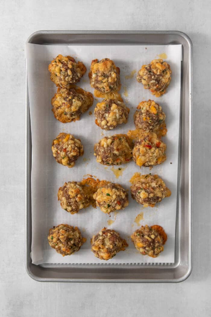 A parchment lined baking sheet holds cooked sausage cheese balls.