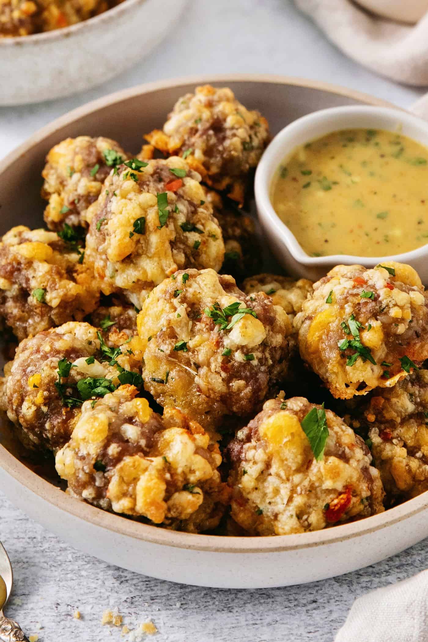 Herb and cheese-flecked sausage cheese balls are ready to be eaten with honey mustard dipping sauce next to them.