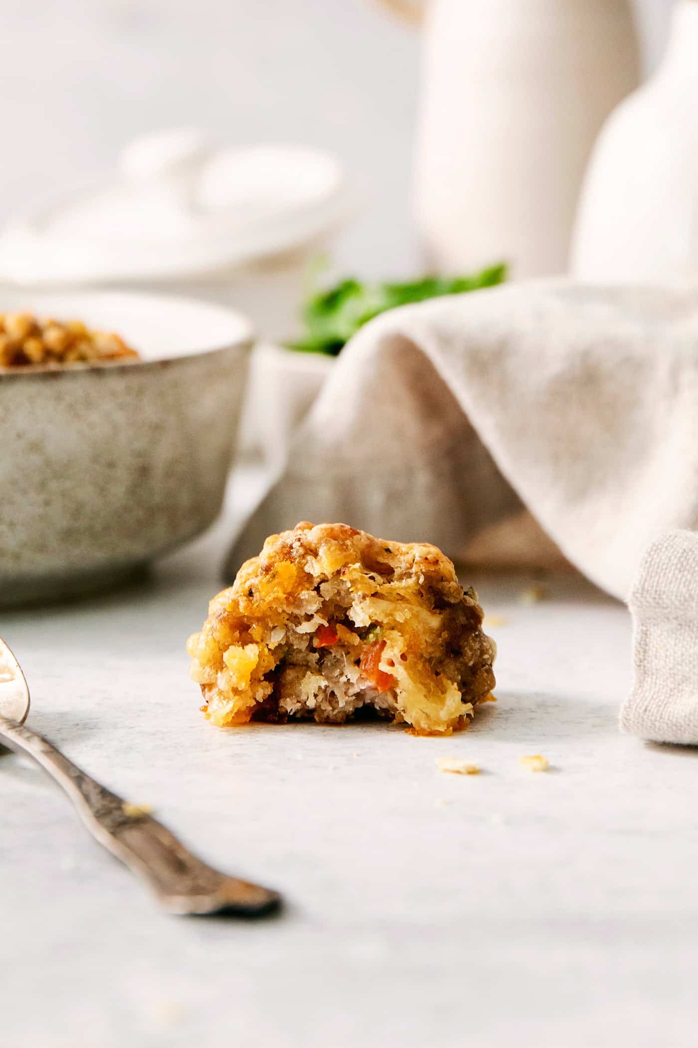 A sausage cheese ball with a bit taken out rests on a white background with a napkin and a fork nearby.