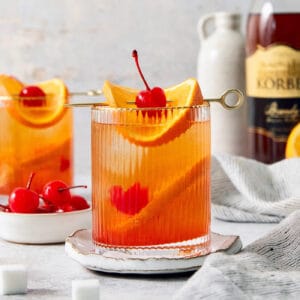 Two glasses of brandy old fashioned are garnish with orange and a cherry.