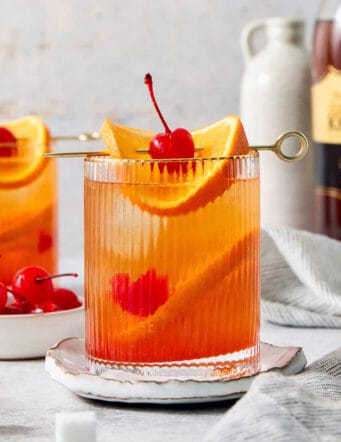 Two glasses of brandy old fashioned are garnish with orange and a cherry.