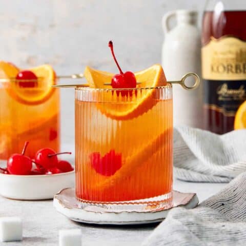 Two glasses of brandy old fashioned are garnish with orange and a cherry.