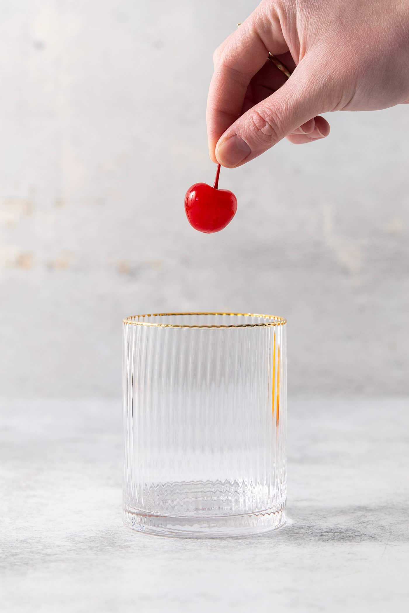 A hand adds a maraschino cherry to a glass.