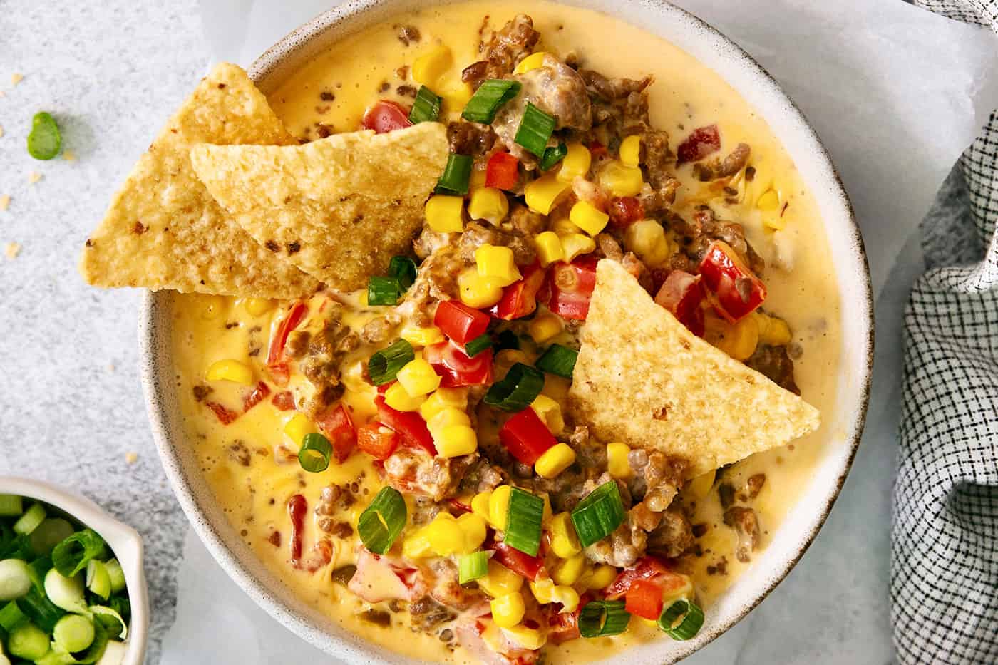 A white bowl of cheesy corn sausage dip is garnished with Rotel and corn chips.