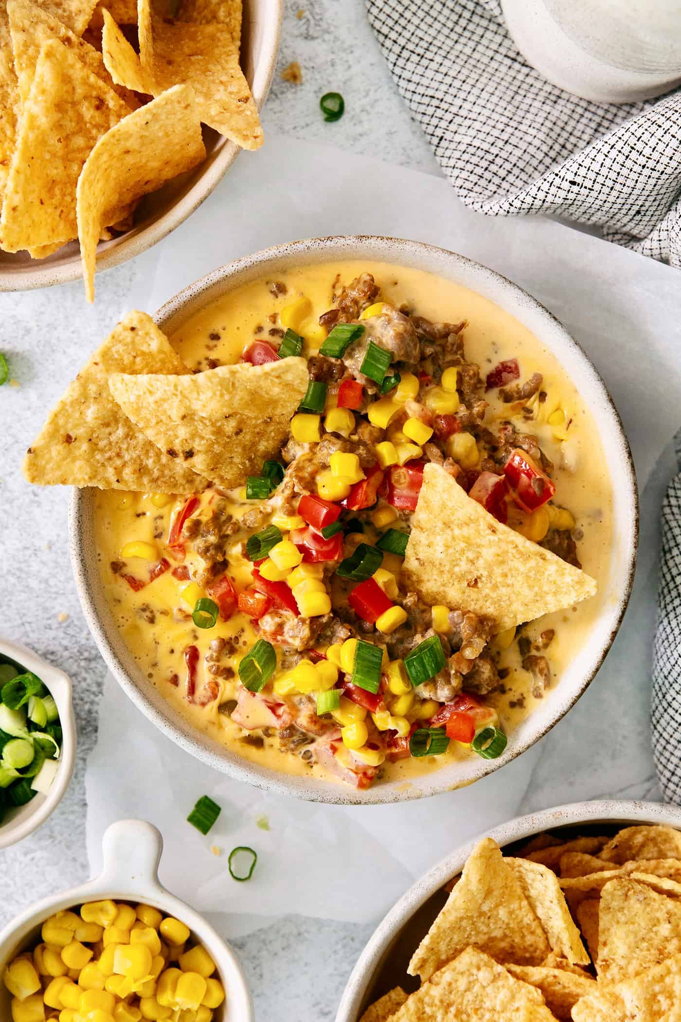 A white bowl of cheesy corn sausage dip is garnished with Rotel and corn chips.