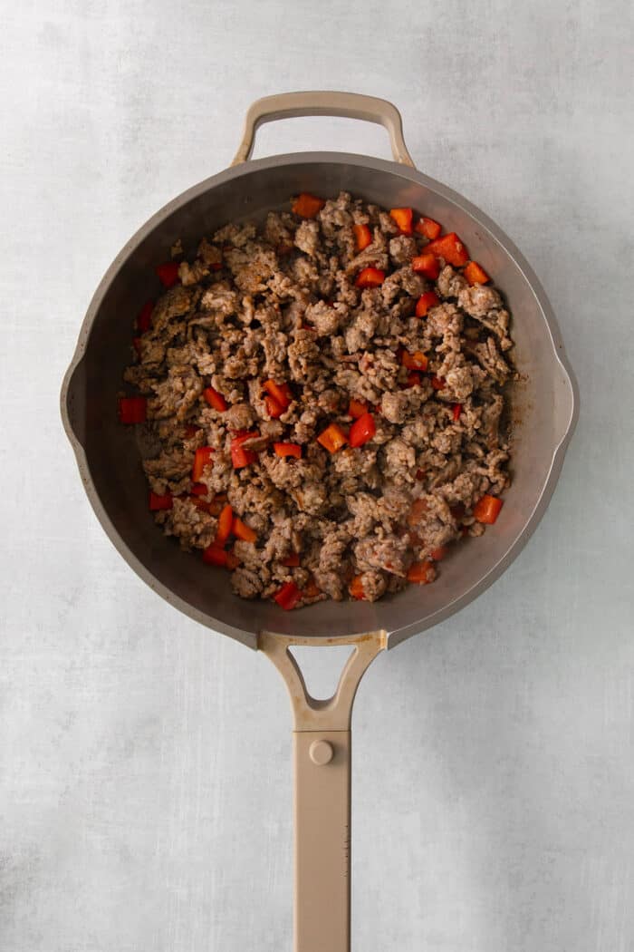 Sausage browns in a skillet with red bell pepper.