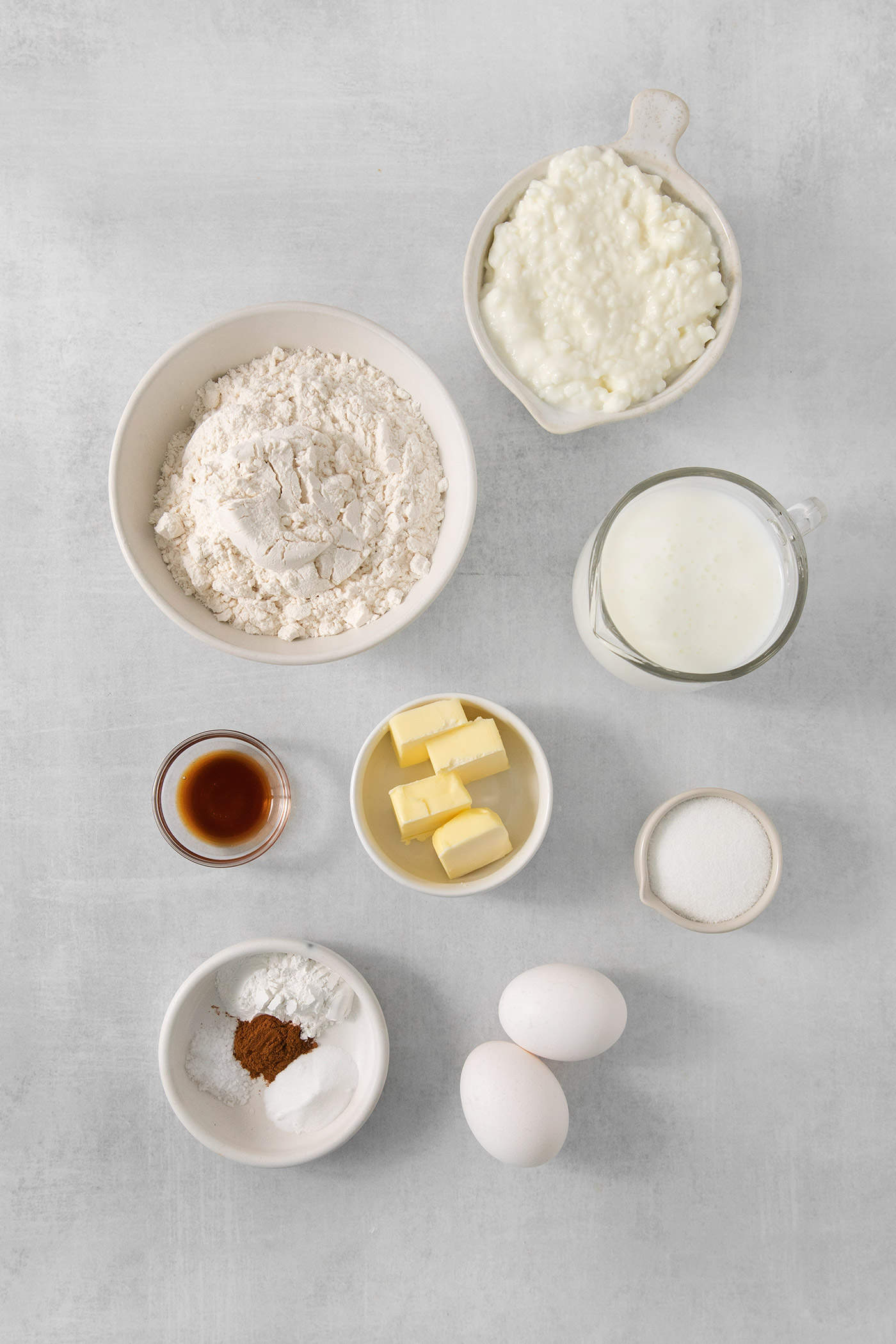 The ingredients for cottage cheese pancakes are shown portioned out: flour, sugar, eggs, buttermilk, cottage cheese, baking powder and baking soda, salt, vanilla, and cinnamon.