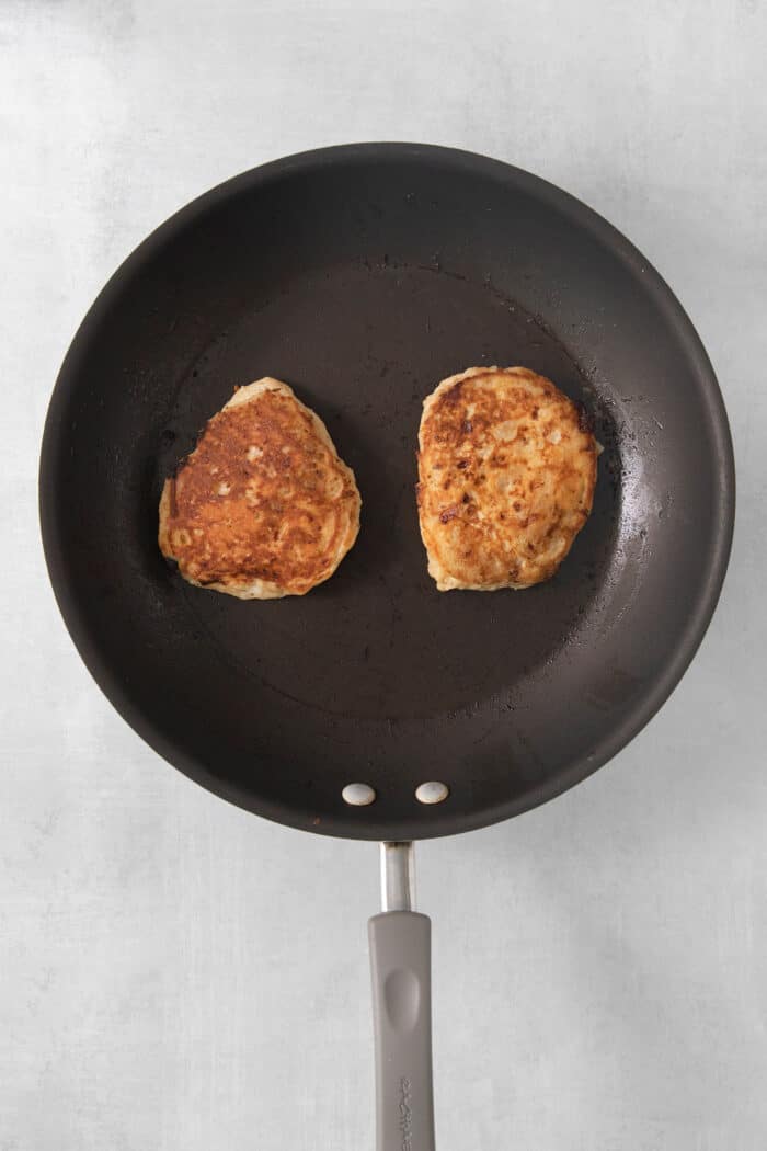 Two cottage cheese pancakes cook in a skillet.