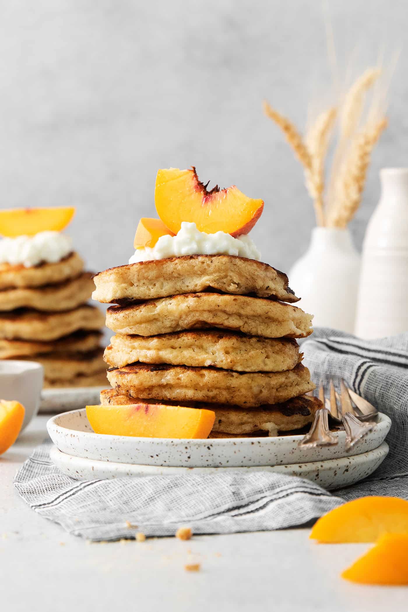 Peach slices and whipped cream top cottage cheese pancakes with more seen in the background.