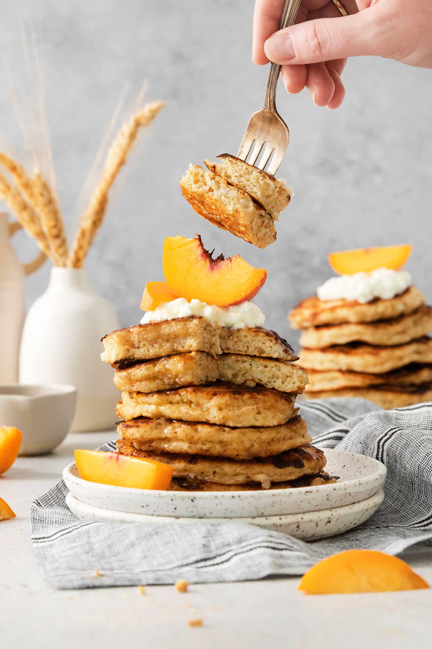 Two bites of cottage cheese pancake are picked up with a fork, with the stack topped with whipped cream and peaches below.