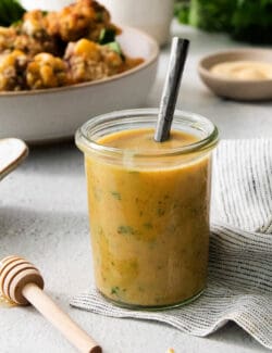 A glass jar holds honey mustard dip with a spoon handle sticking out.