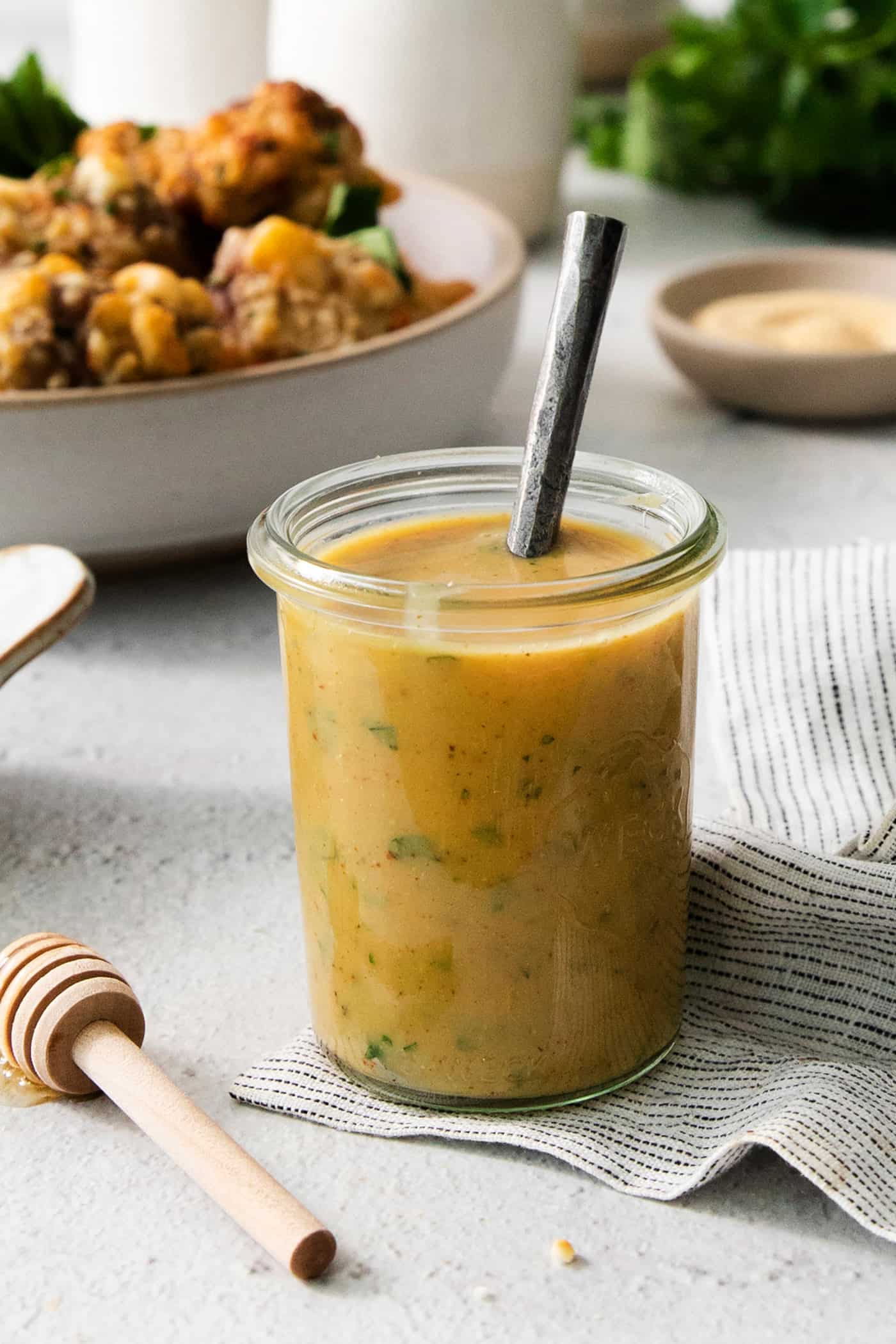 A glass jar holds honey mustard dip with a spoon handle sticking out.