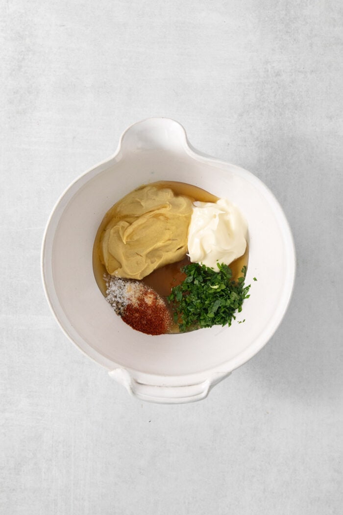 Honey, mayonnaise, parsley, mustard, and spices are shown in a white bowl.