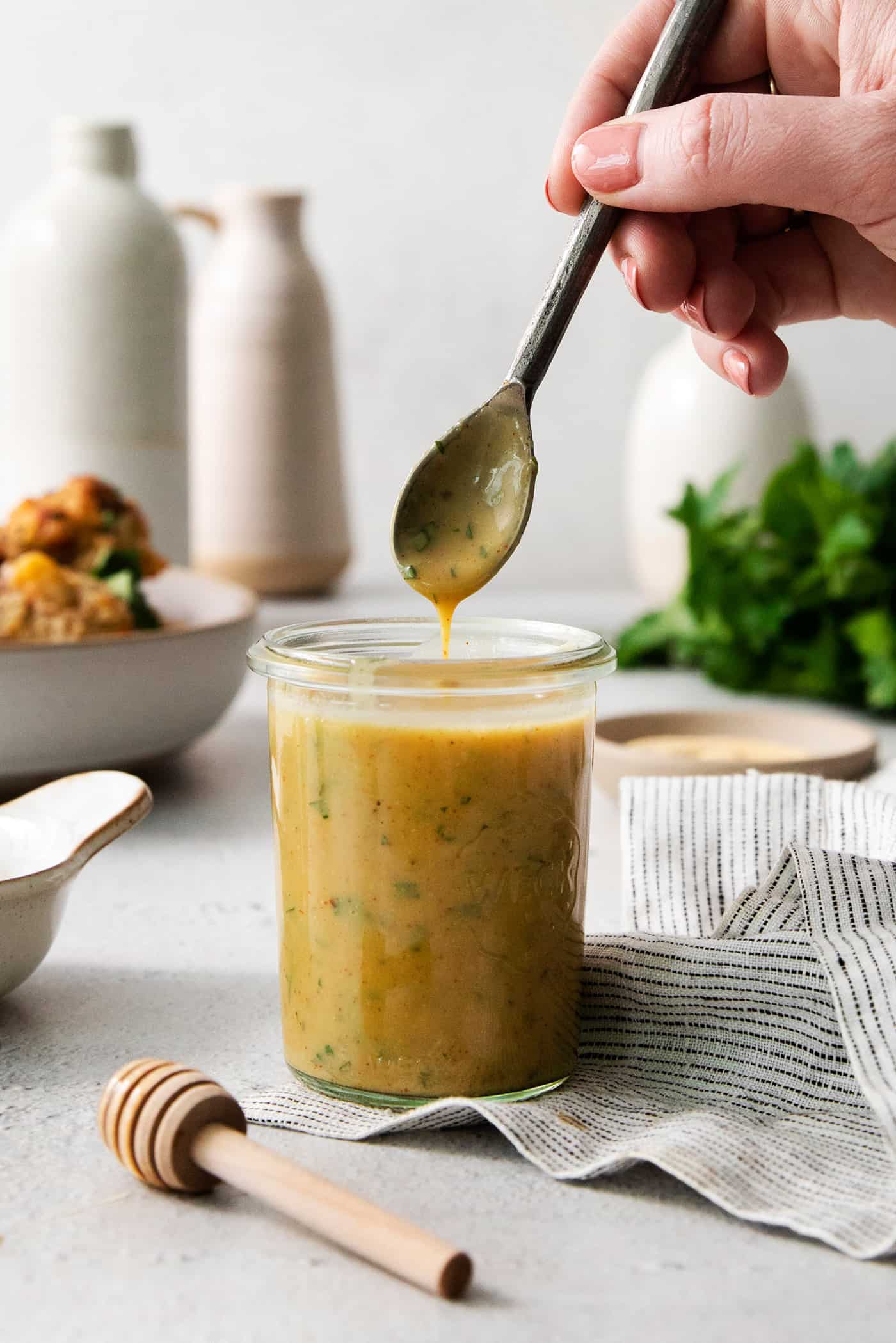 A hand dips a spoon into a glass jar of honey mustard dip