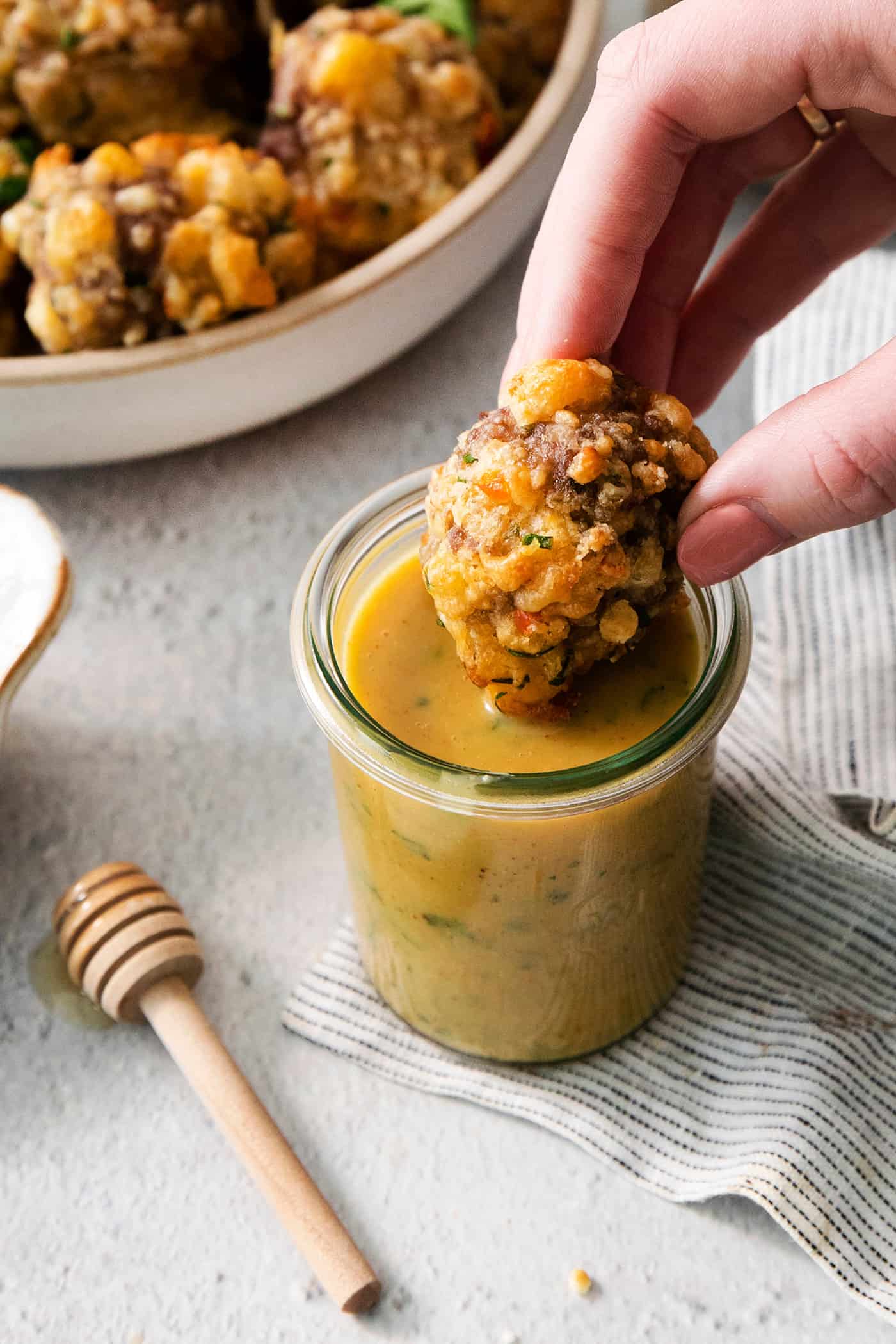 A sausage cheese ball is dipped into a jar or honey mustard dip.