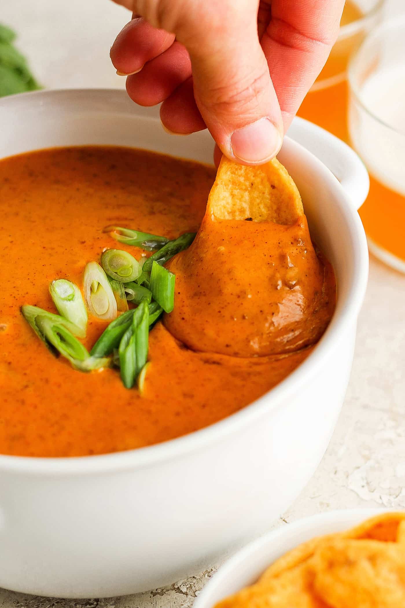 A hand dips a chip into a bowl of chili cheese dip.