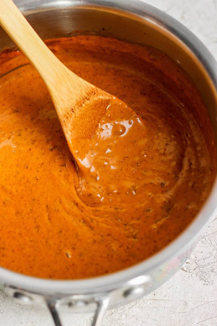 A wooden spoon stirs chili cheese dip in a pot.