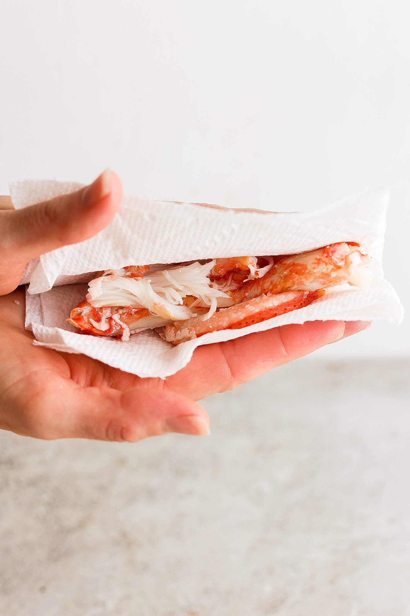 A hand holds a paper towel folded over shrimp and crab to dry them.