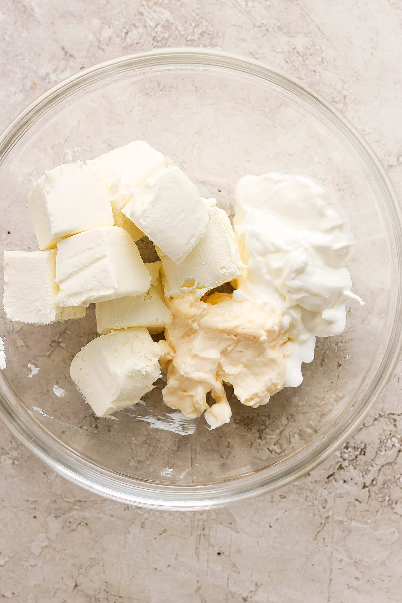 Chunks of cream cheese and sour cream are placed in a clear bowl.