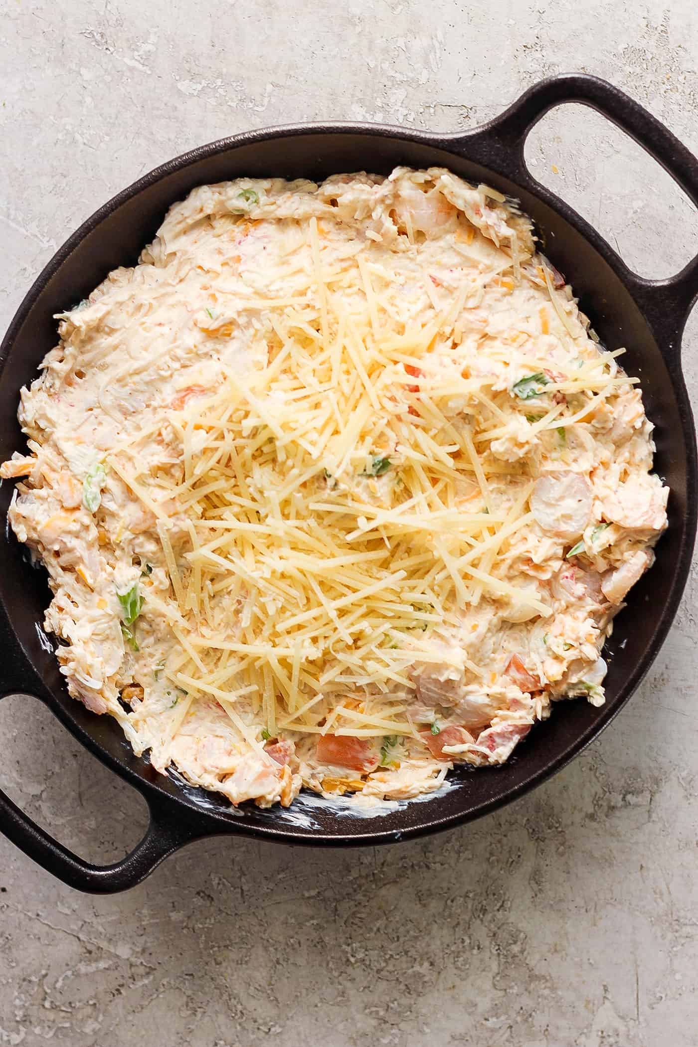 A pan of uncooked shrimp and crab dip is topped with shredded cheese.