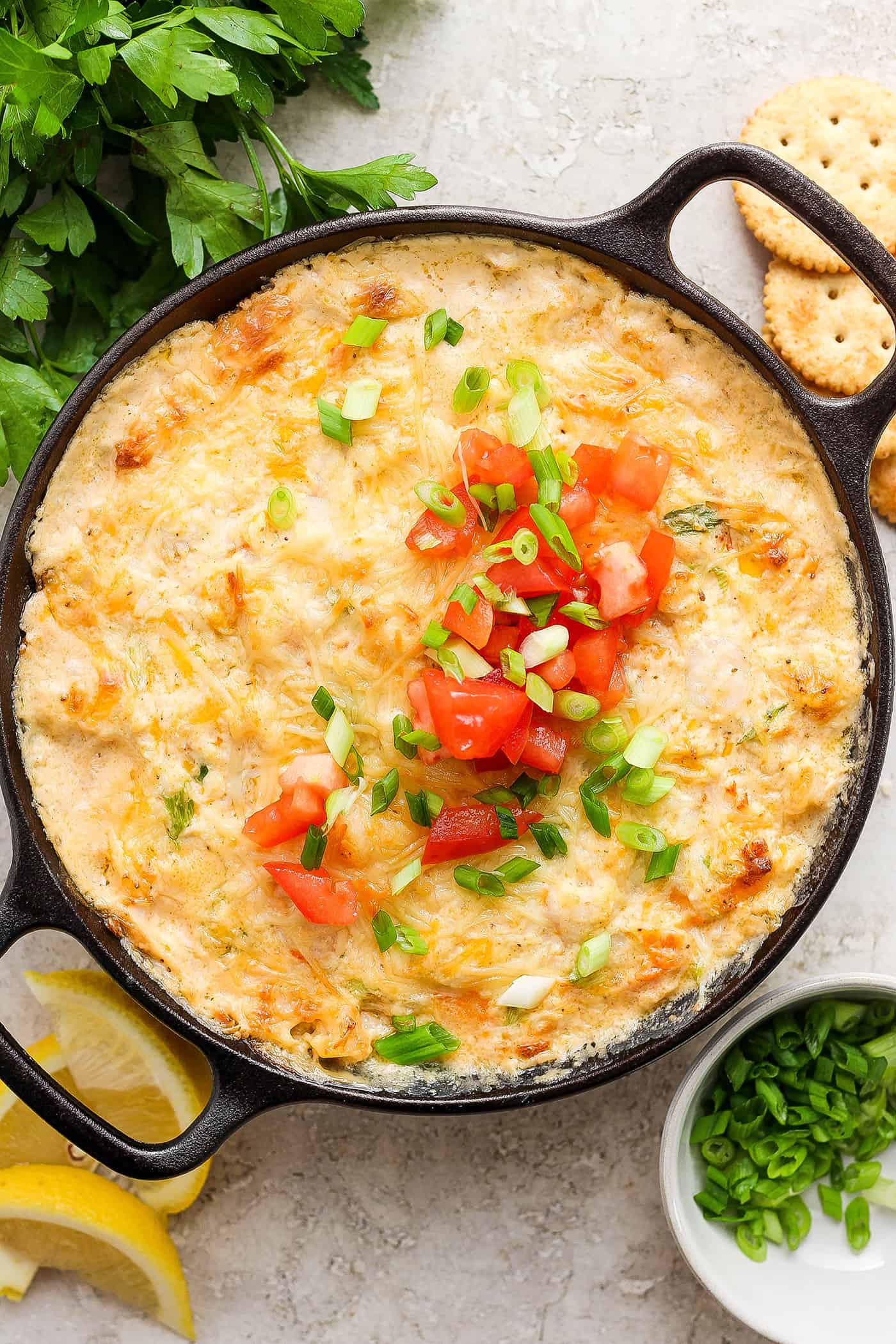 A cast iron pan holds baked shrimp and crab dipped garnished with chopped tomatoes and green onions.