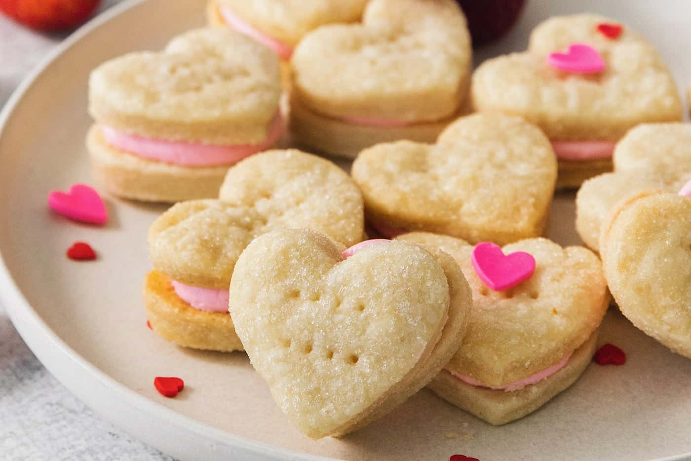Heart-shaped strawberry cream wafer cookies are displayed on a white plate.