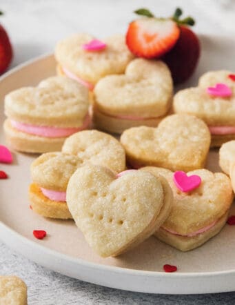 Heart-shaped strawberry cream wafer cookies are displayed on a white plate.