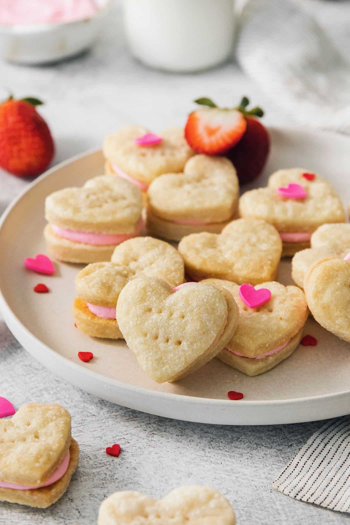 Heart-shaped strawberry cream wafer cookies are displayed on a white plate.