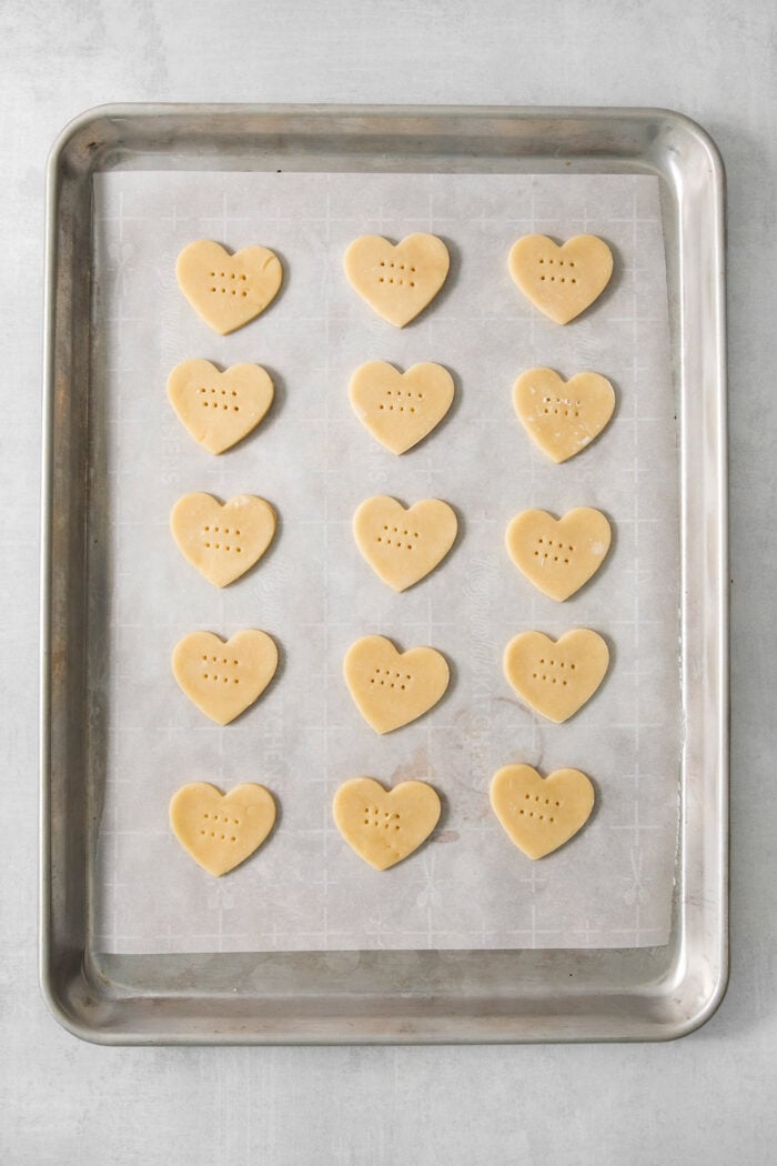 Fifteen heart shaped cream wafer cookies are arranged on a cookie sheet.