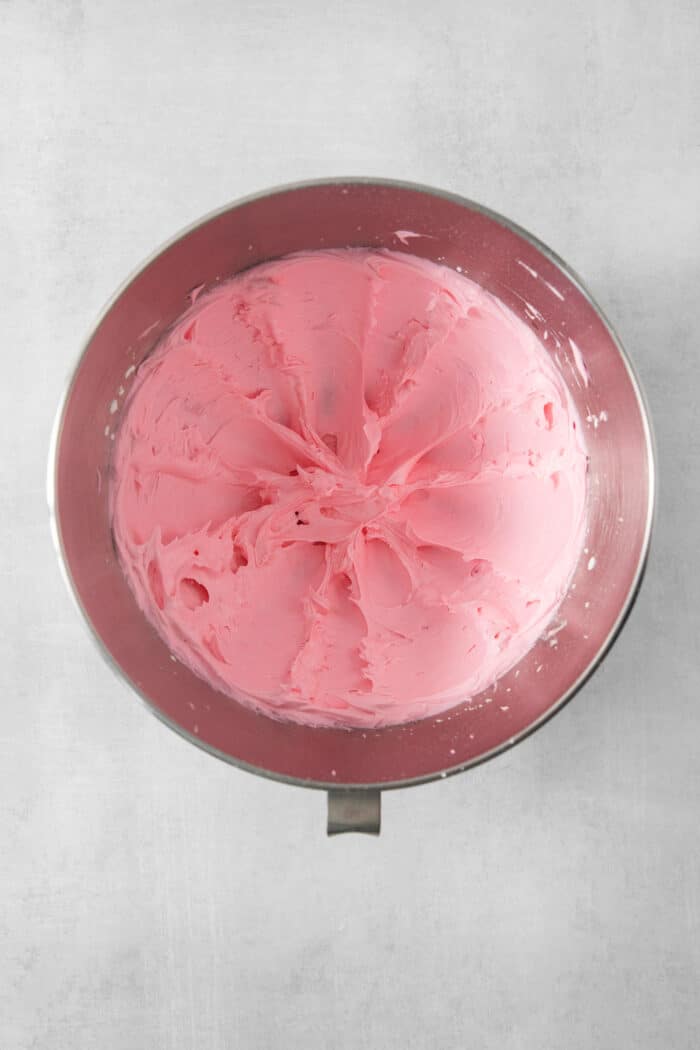 A metal bowl full of pink strawberry buttercream.